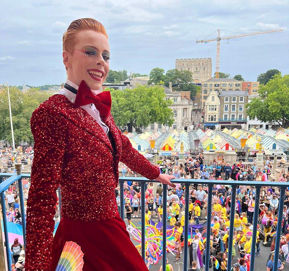 Korben wears a red dress/tuxedo combination for Norwich Pride 2022