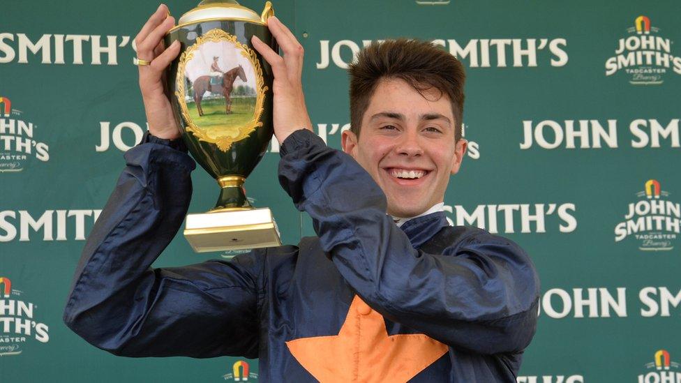 Man in jockey silks lifts a trophy