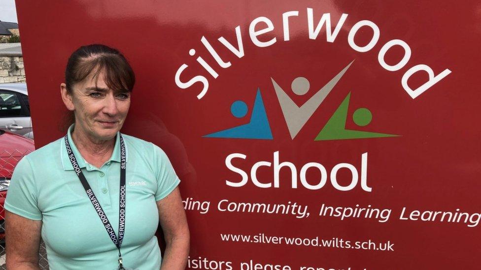 Siobhan Cheadle, head of learning at Silverwood school, Trowbridge campus. She has dark hair which is in a ponytail. She is wearing a mint green polo shirt with a Silverwood School black lanyard around her neck. She is stood in front of a red sign which reads 'Silverwood School' in white text.