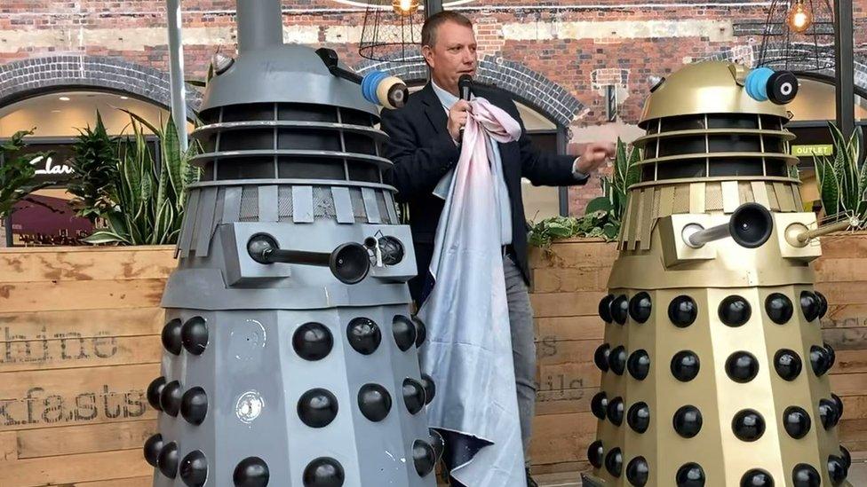 Man stands in between two daleks, replicas of the famous villains seen on Doctor Who.