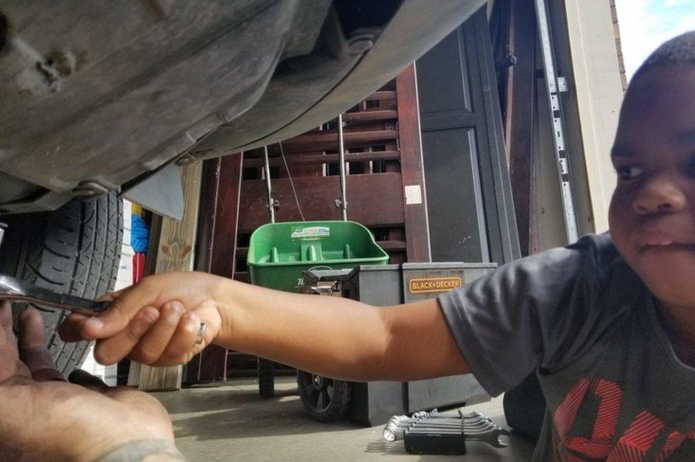 Tysen reaches out underneath his mum's car, with a helping hand from Adam