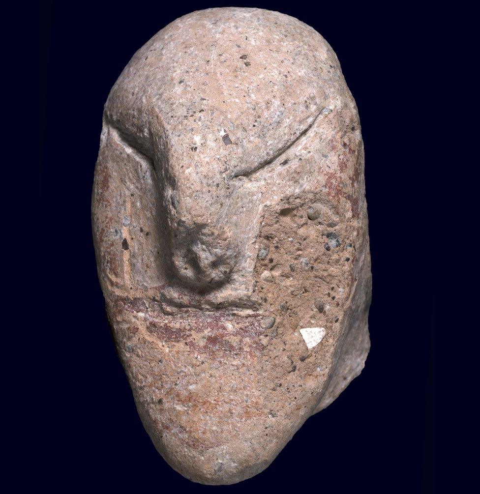 A close up image of a small stone figurine depicting a person's head