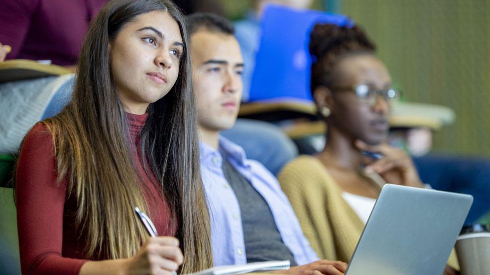 Two female and a male student sitting in a lecture hall, looking forward and taking notes