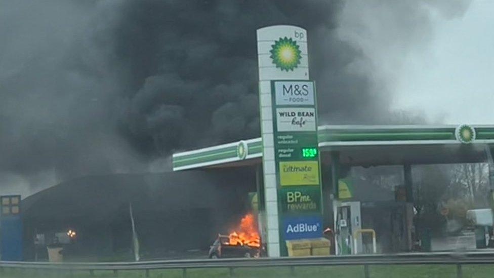 Plumes of black smoke coming from a car and its bonnet appears to be on fire