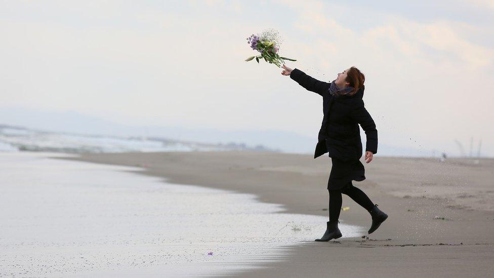 A woman throws a flower bunch at Fukanuma beach on March 11, 2016 in Sendai, Japan