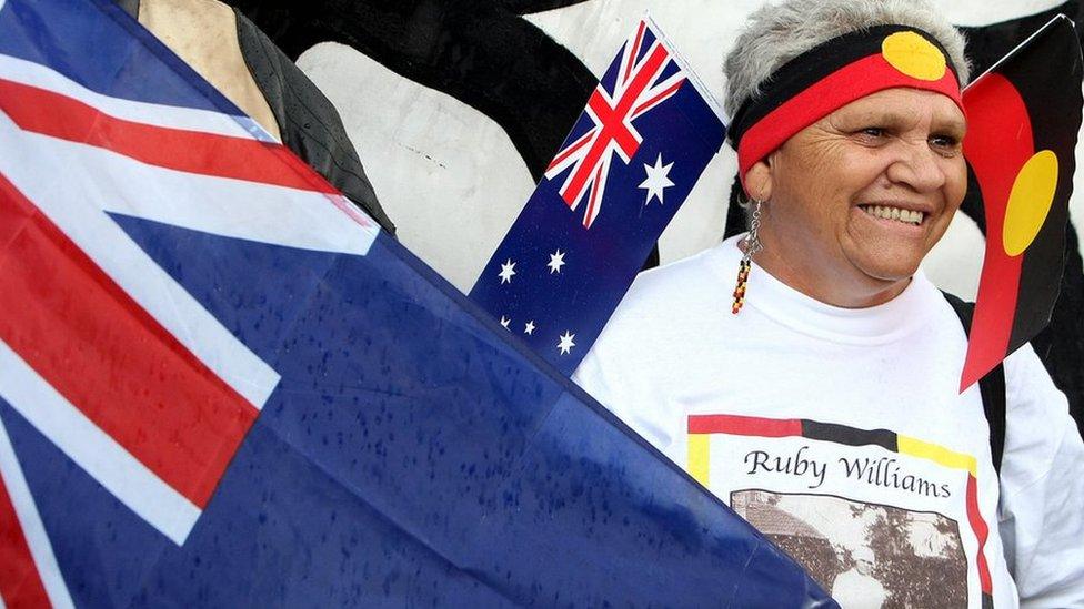 An Australian Aborigine holds the Australian national flag and the Aboriginal and Torres Strait Islander flag