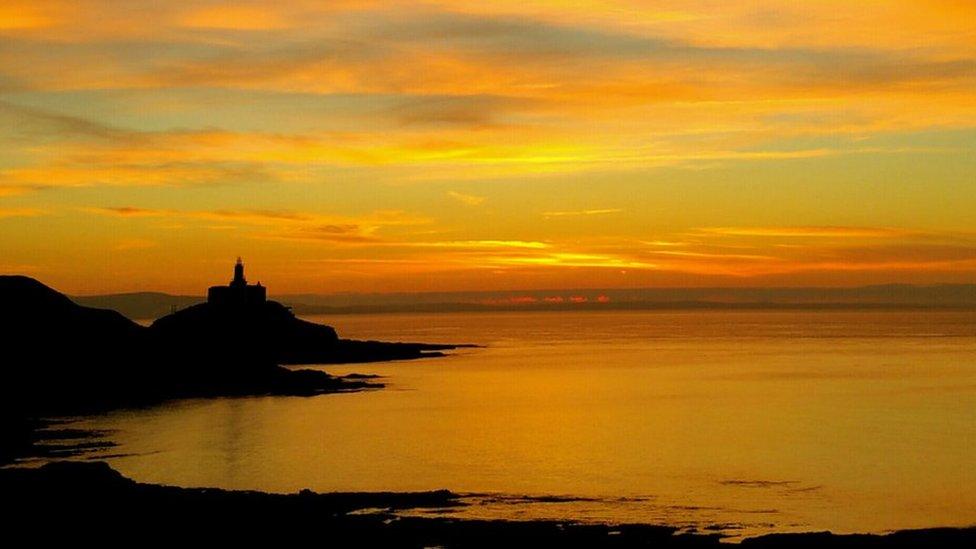 An amber sunrise over Mumbles Lighthouse