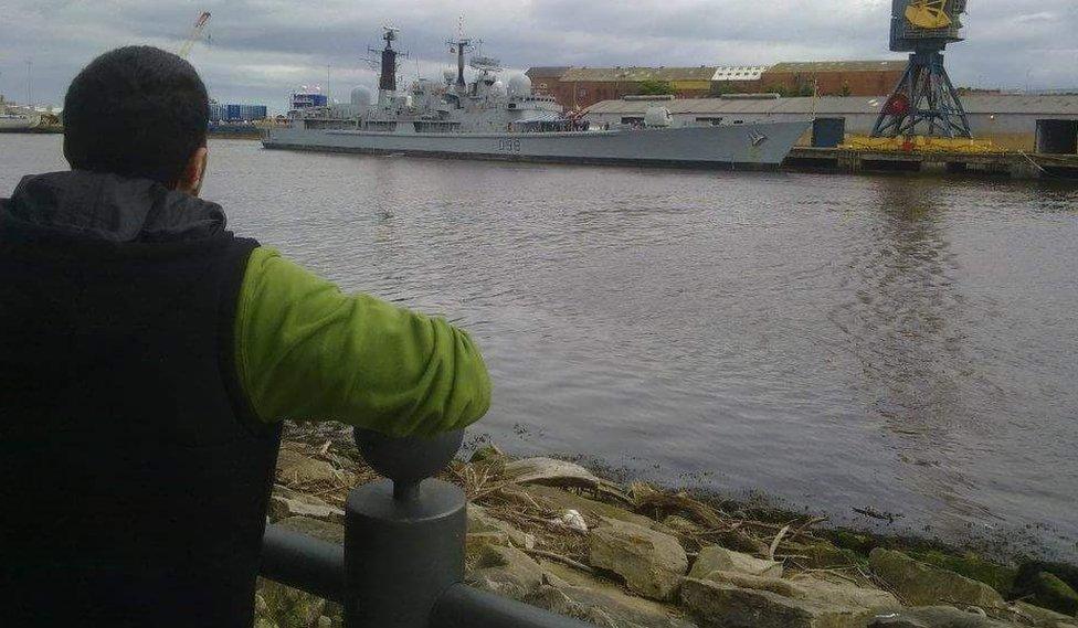 A picture of Jehad Fadda with his back to the camera, leaning on a railing and looking out over a river