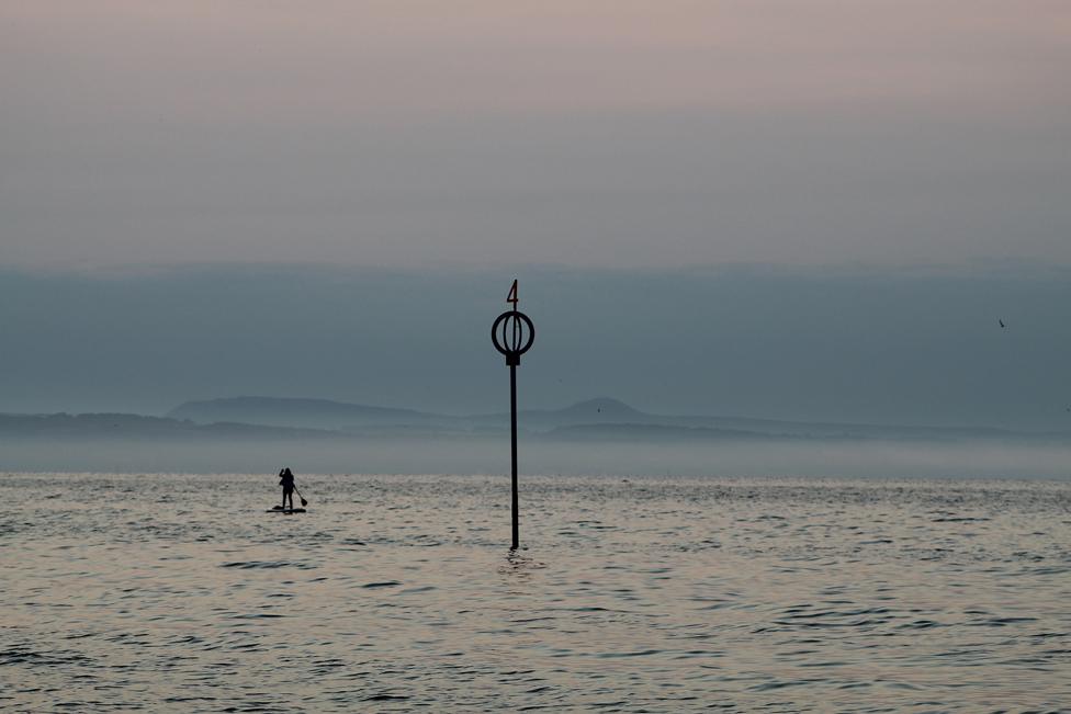 At the End of the Day - a paddleboarder at sea, next to a metal structure sticking out of the water