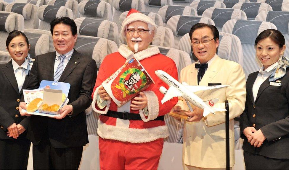 Japan Airlines President Yoshiharu Ueki (2nd L) and Masao Watanabe (2nd R), President of KFC Japan pose with a statue of Colonel Sanders (C) wearing a Santa Claus costume at a press conference to announce plans to offer in flight KFC for 3 months from December 2012