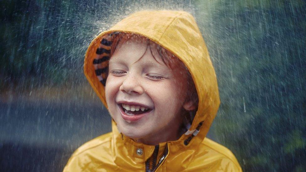 Little boy in raincoat smiles as it rains