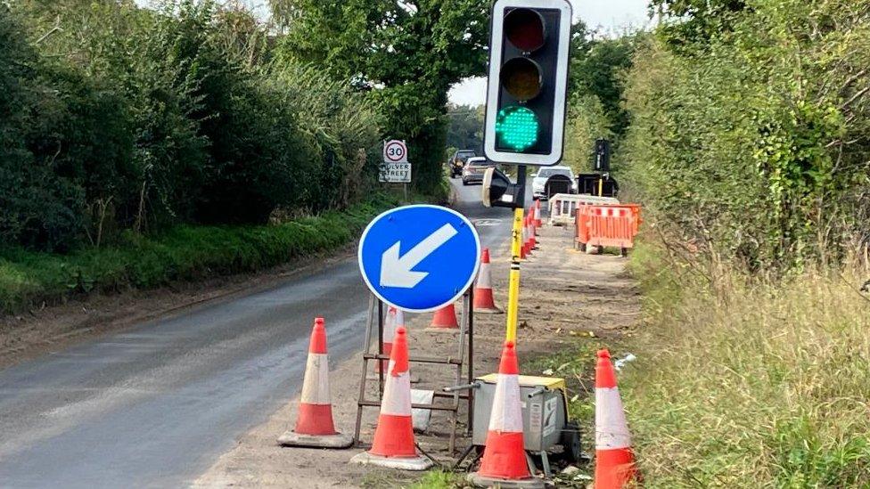 Temporary traffic light, diversion sign and road cones on a road