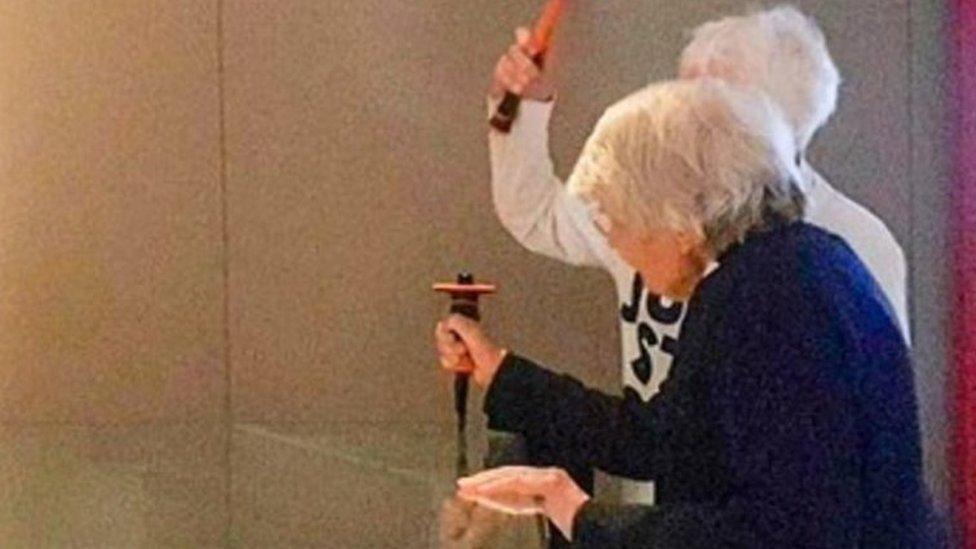 Two women, with one lifting up a hammer as the other holds a chisel on glass covering the Magna Carta