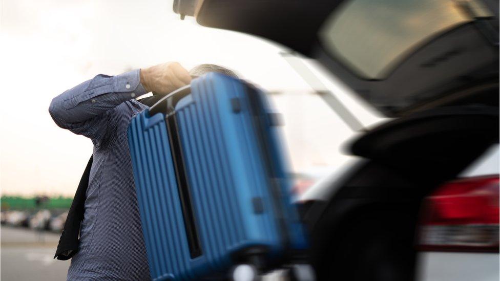 man removing suitcase from back of car