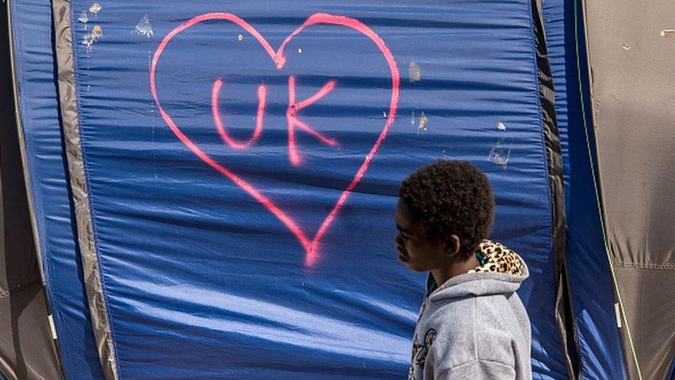 A migrant walks next to a tent tagged with the initials of the UK in the camp for migrants and refugees in Calais