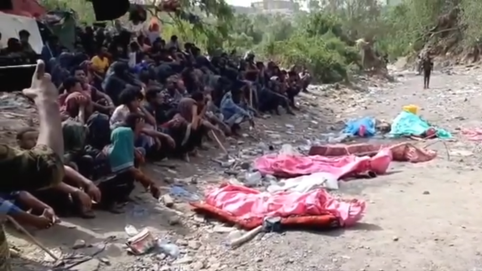 Migrants look at covered bodies during a burial on the Saudi-Yemeni border