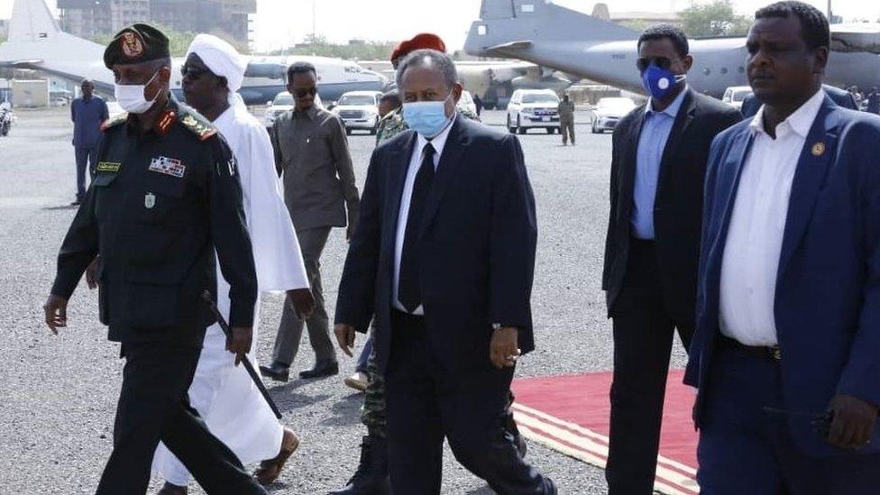 Prime Minister of Sudan, Abdalla Hamdok (C) wears a face mask as a preventive measure against the coronavirus (Covid-19) pandemic as he attends the official funeral ceremony of Sudan's Defense Minister Gamal Omer, 59, died in Juba, the capital of neighboring South Sudan, at Khartoum International Airport on March 25, 2020 in Khartoum