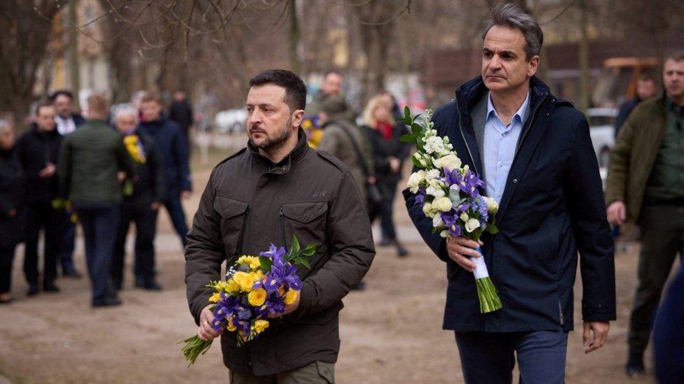 Volodymyr Zelenskiy and Kyriakos Mitsotakis visit a makeshift memorial to victims of a previous drone strike