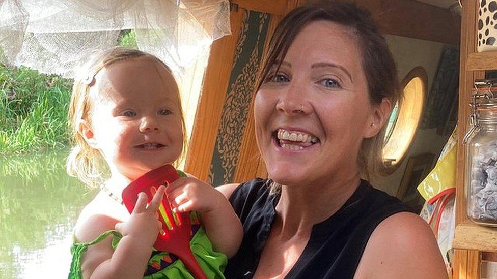 Mary Maw holding daughter Sybil next to their kitchen window on boat "Adrastea"