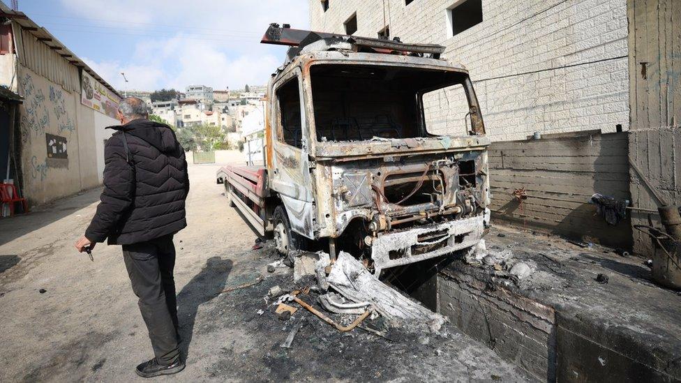 A Palestinian man inspects a burned-out lorry in Hawara, in the occupied West Bank, after an attack by Israeli settlers (28 March 2023)