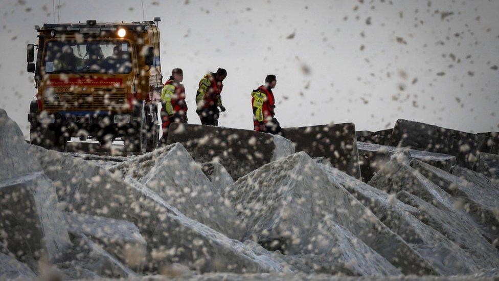 Emergency services members stand on a beach after a group of surfers was reported in trouble at the Noordelijk Havenhoofd