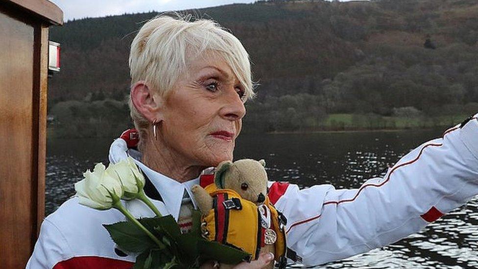 Gina Campbell holding flowers and her father's mascot, Mr Whoppit, onboard a boat on Coniston Water on the 50th anniversary of his death