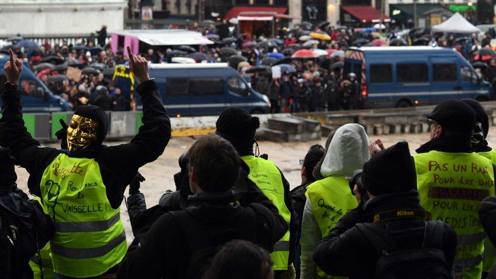 Yellow vests watch as red scarves march through Paris. 27 Jan 2019