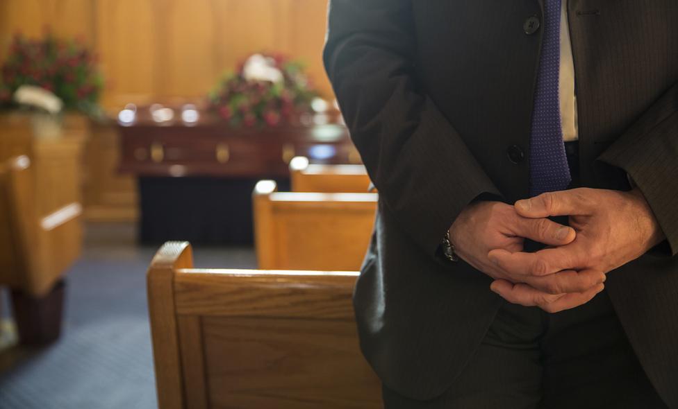 Man standing, coffin in background