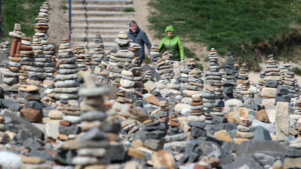 People walk by pebble stacks