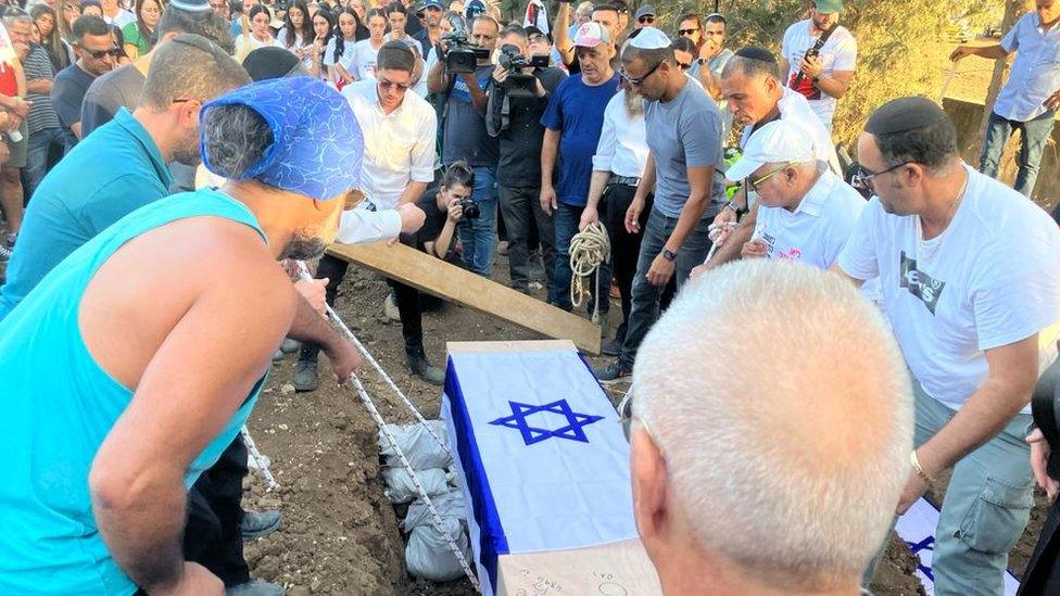 A coffin is lowered into a grave watched on by mourners