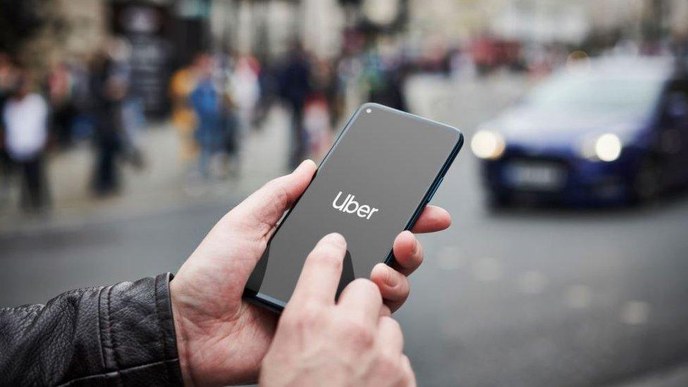 A man using the Uber app by a busy London road