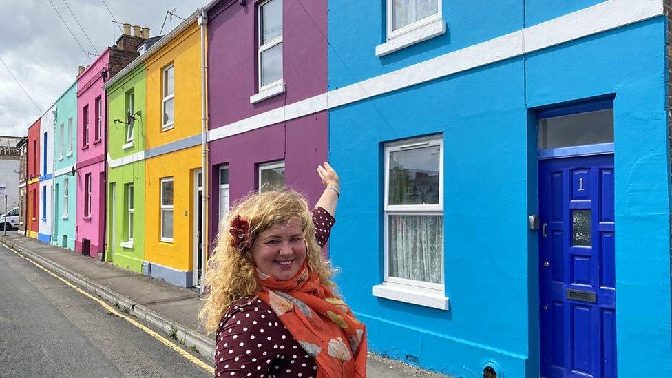 Woman stands in front of colourful houses