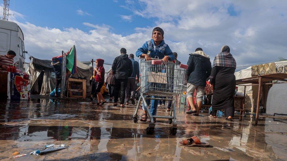 Boy walks over a large rain puddle after rainstorms in Khan Yunis, 15 November 2023