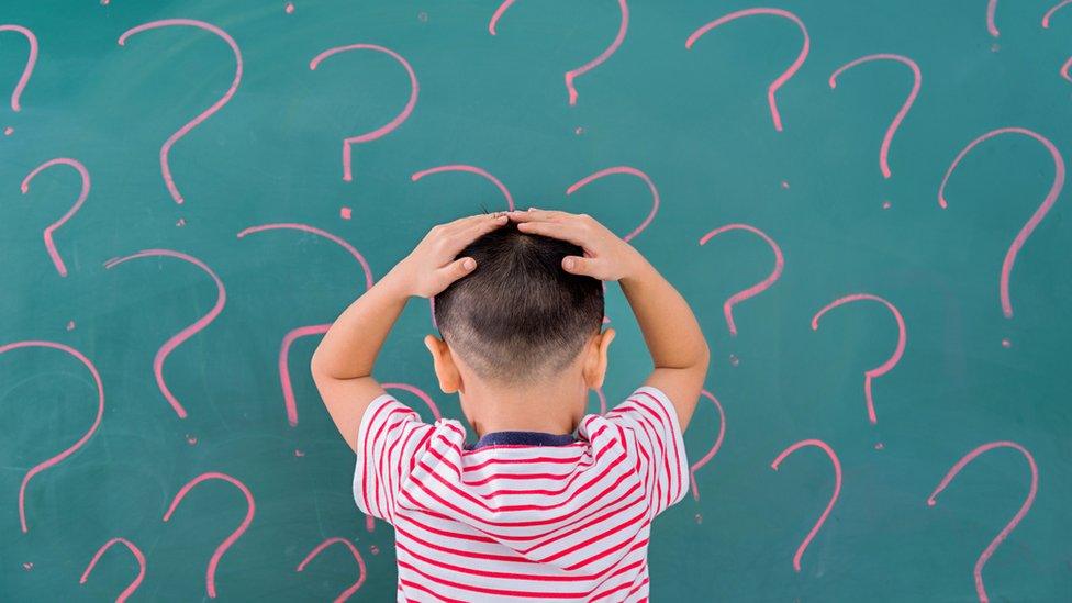 boy looking at blackboard covered in question marks