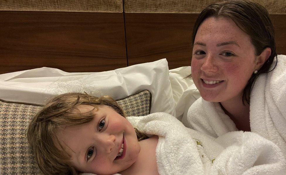 Kiera Moran and her son Noah smiling on a hotel room bed