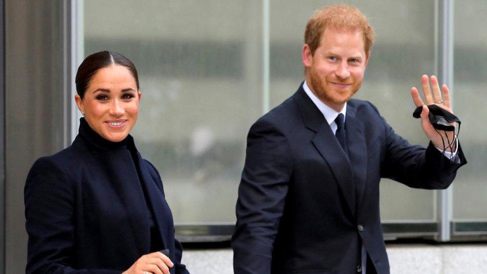 Meghan Mark and Prince Harry waving as they leave a building.