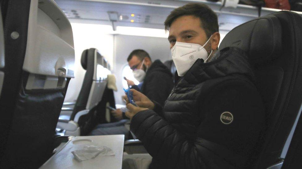 A man wearing a face mask sitting on a plane about to depart from Heathrow Airport