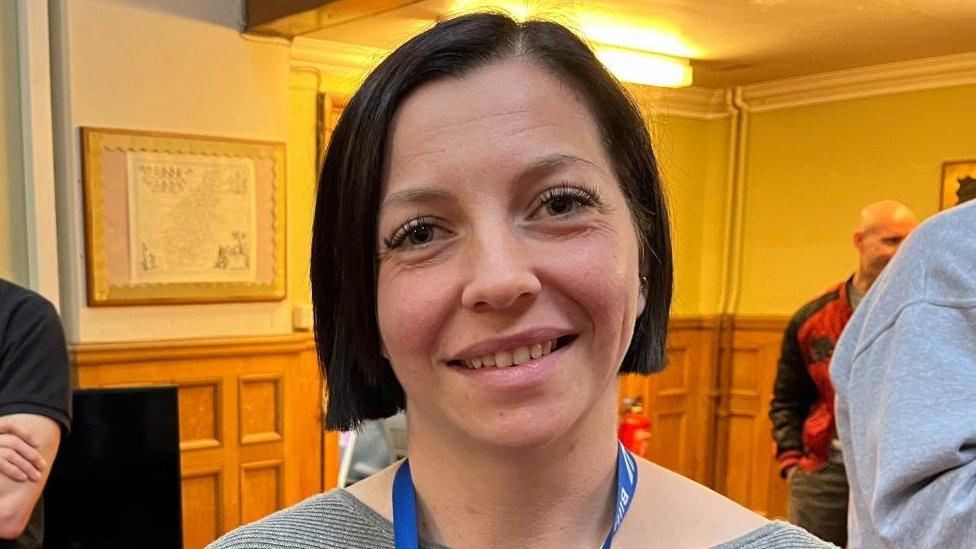 Woman with short black hair wearing lanyard in a wood-panelled meeting room