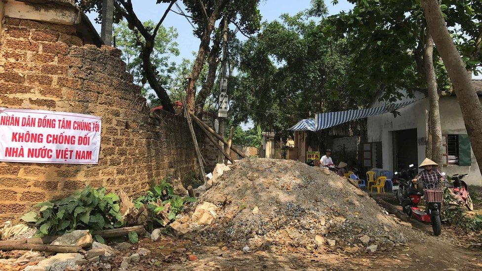 A villager pushes her electric bike on a road partially blocked by rocks, wood and debris inside Dong Tam commune in My Duc district on the outskirts of Hanoi on 20 April 2017