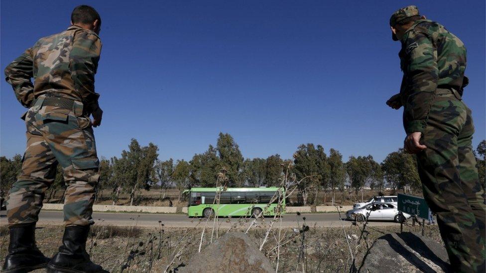 Syrian Army forces look on as buses leave district of Waer during a truce between the government and rebels, in Homs