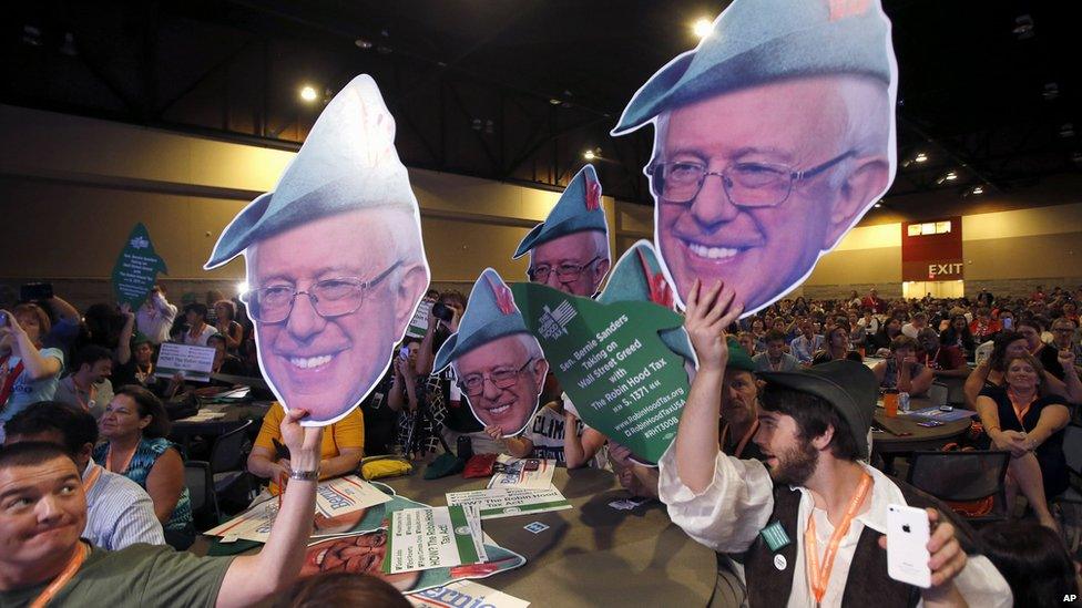 Supporters hold up signs featuring the Bernie Sanders's face.