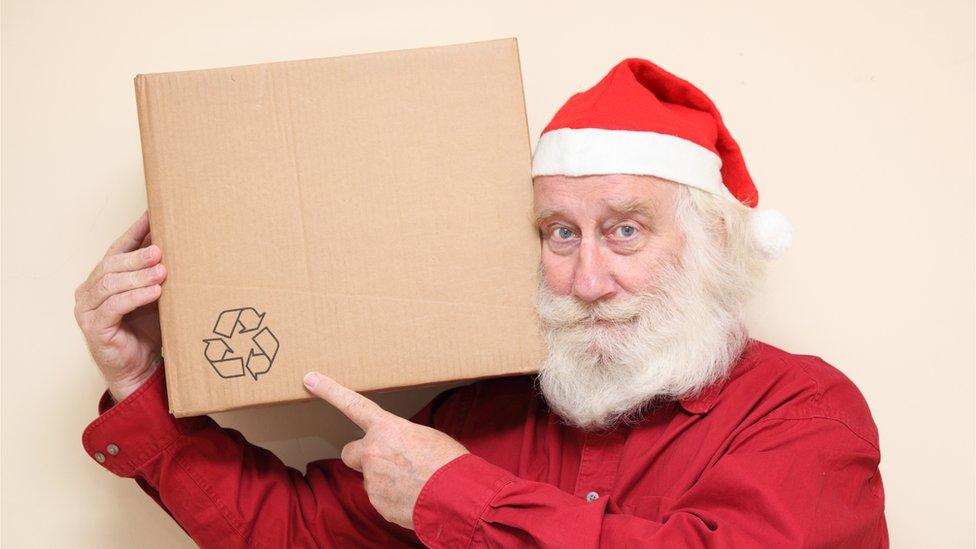 portrait of a kindly man with a white beard in a santa hat - carrying a large cardboard box, happy to be recycling