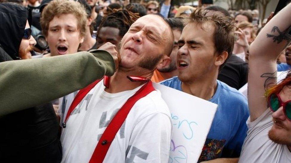 A man wearing a shirt with swastikas is punched by a member of a crowd of protesters at University of Florida's campus, where white nationalist Richard Spencer gave a speech.