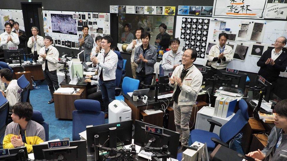 Jaxa scientists and staff smile and clap their hands from mission control