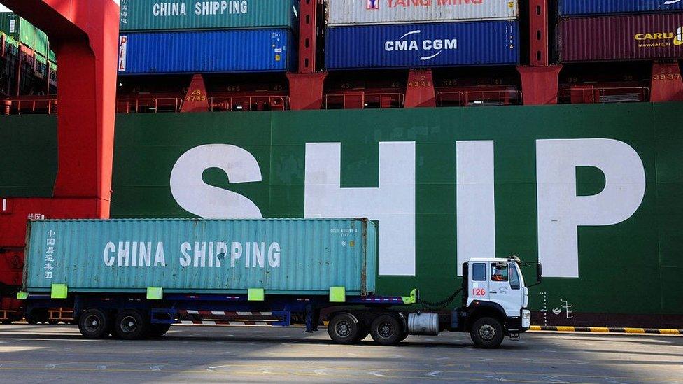 A truck carries a container past a ship at the port in Qingdao, in China's Shandong province