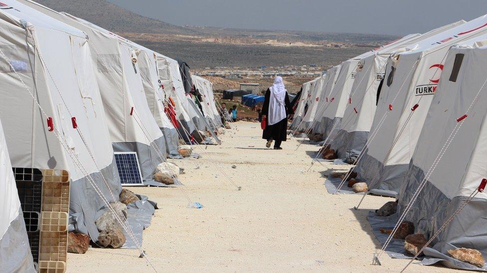 A Syrian woman, evacuated from the Eastern Ghouta, walks between tents at a camp for displaced people in Kafr Lusin, in Idlib province, on 1 April 2018