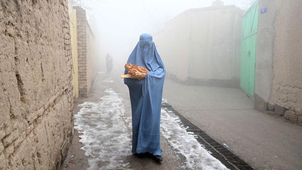 a woman in a burqa walks through a street holding a parcel of food