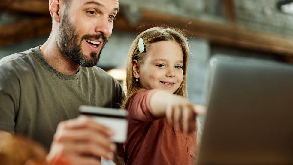 Father using credit card while shopping online with his daughter over a computer at home.