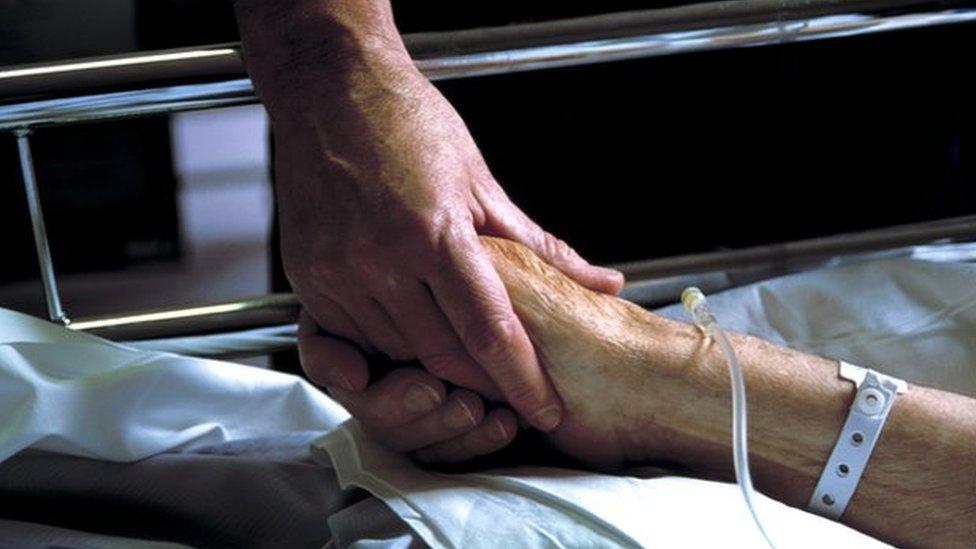 Close up of hand holding the hand of an elderly patient with an IV drip