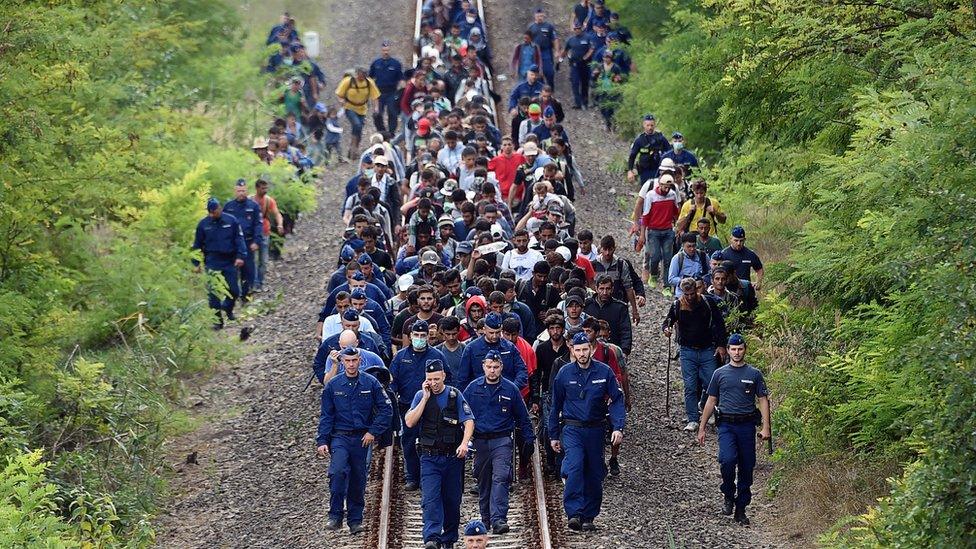 Refugees of different countries accompanied by police officers walk on the railway tracks near Szeged town as they broke out from the migrant collection point near Roszke village of the Hungarian-Serbian border on September 8, 2015